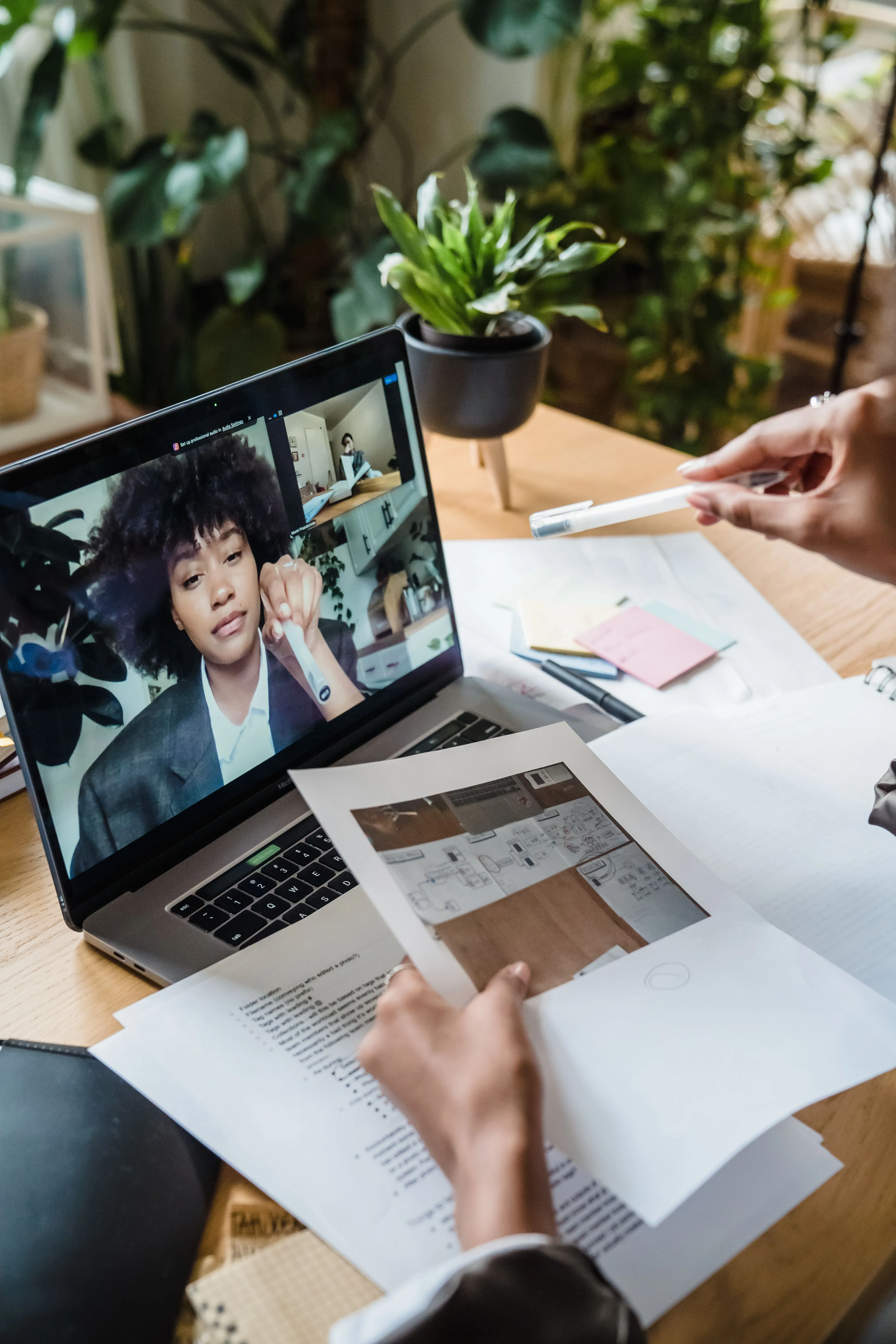 An HR interviewer reviewing printed notes at a desk while a candidate speaks on a laptop video call.