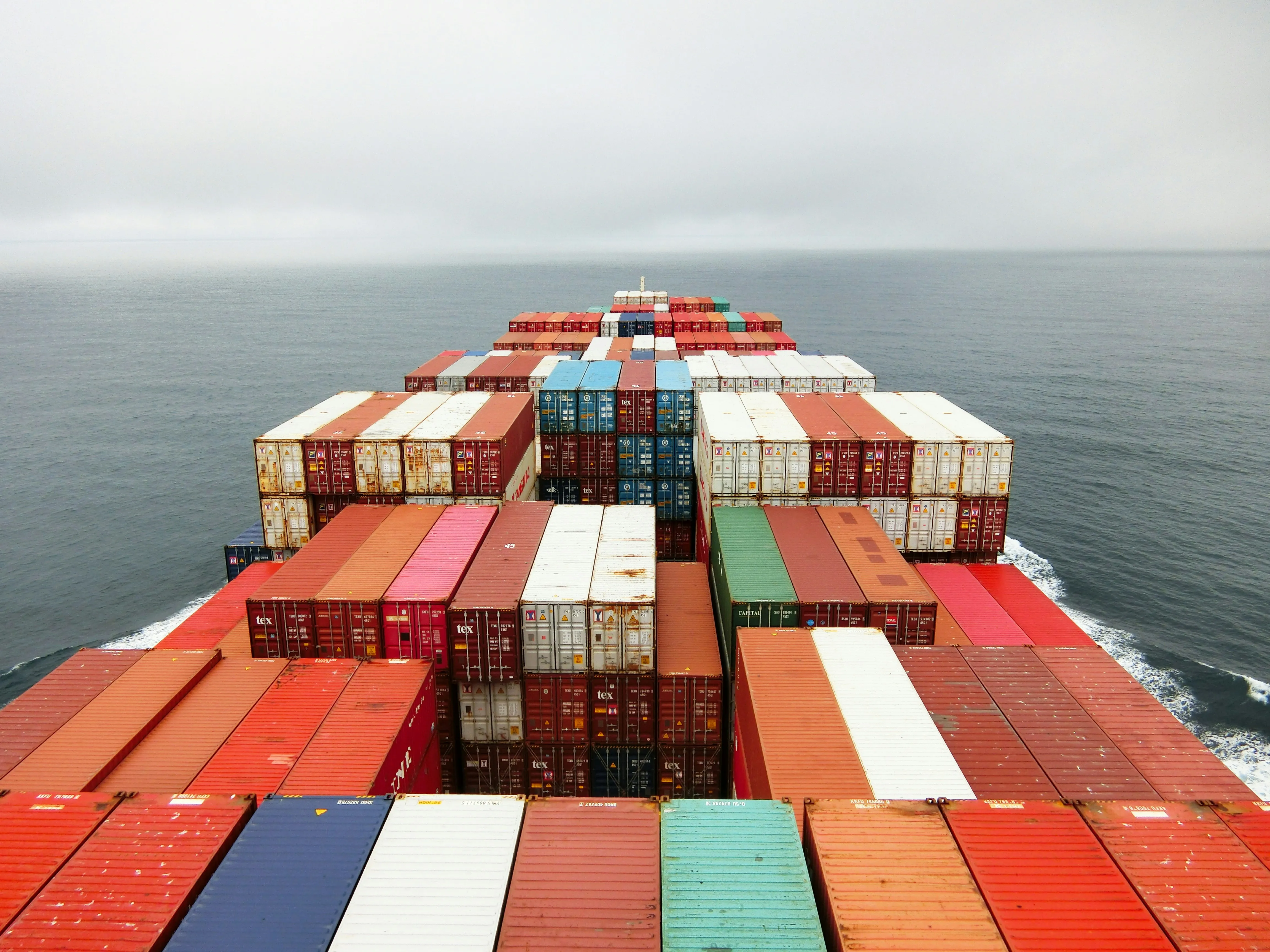 Stacked shipping containers filling the deck of a cargo vessel at sea.