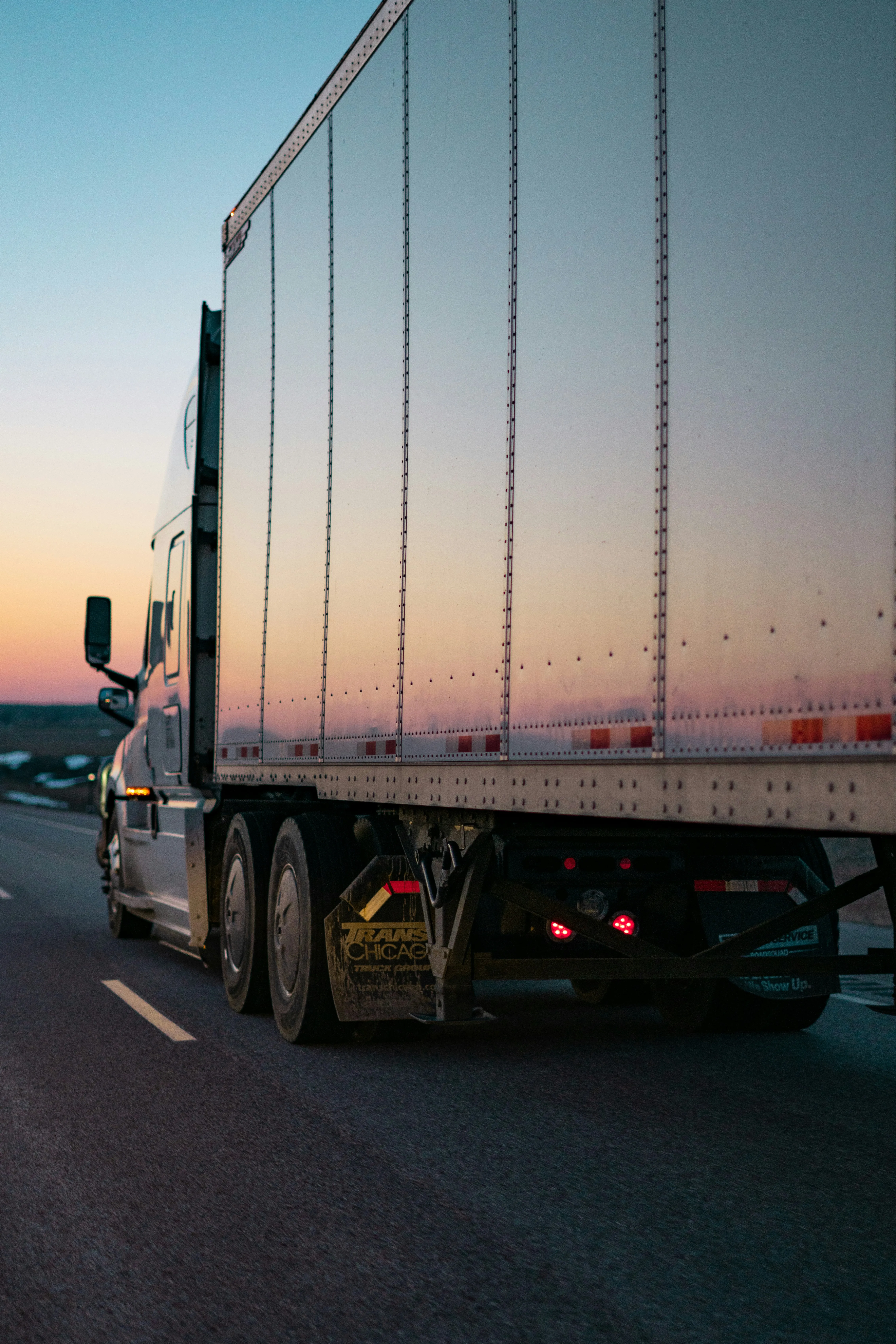 An articulated truck and trailer on an open highway at dusk.