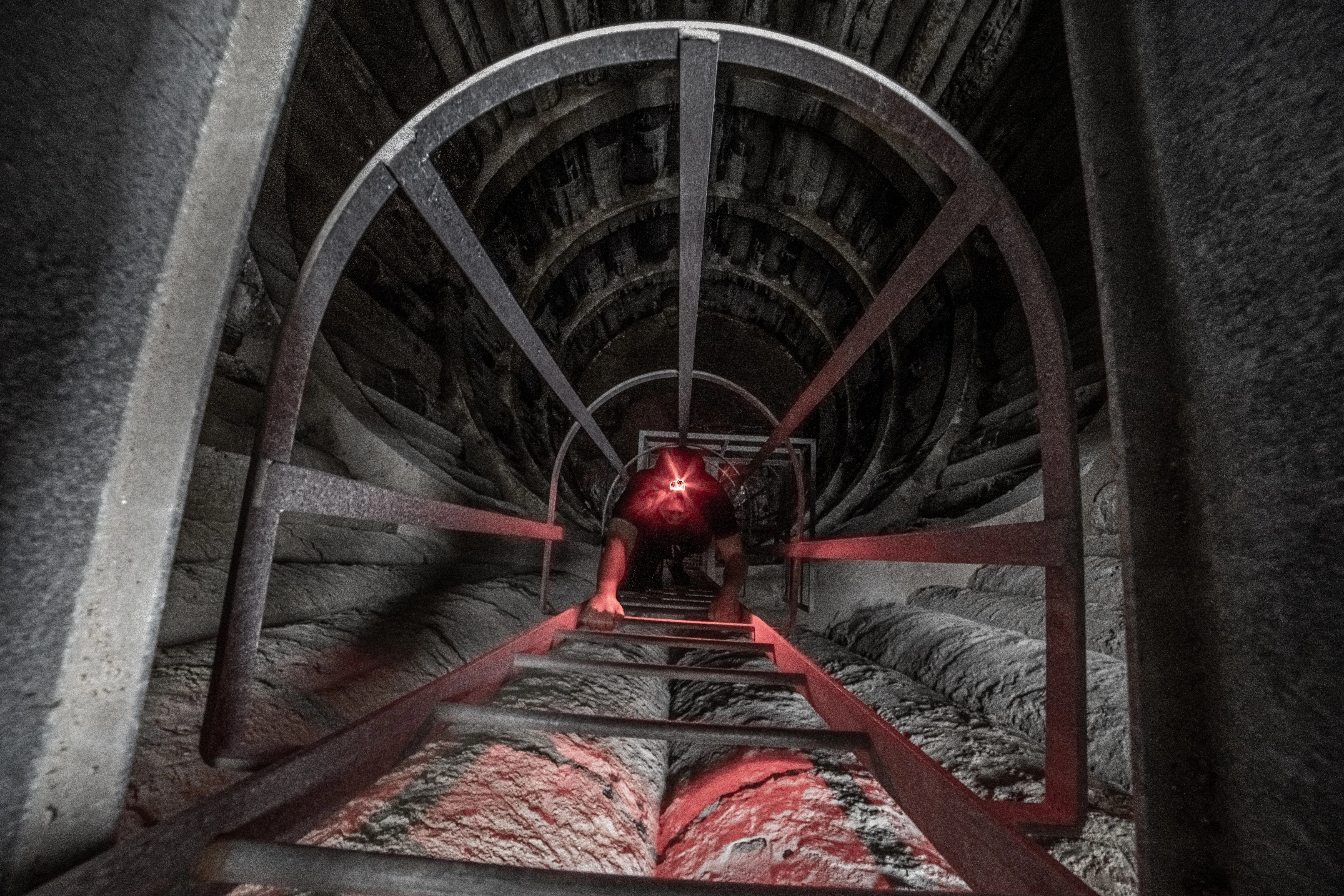 A worker climbing an internal ladder inside a dimly lit industrial silo.