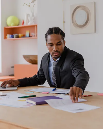 A business owner working alone at a large desk, laying out paperwork beside an open laptop.