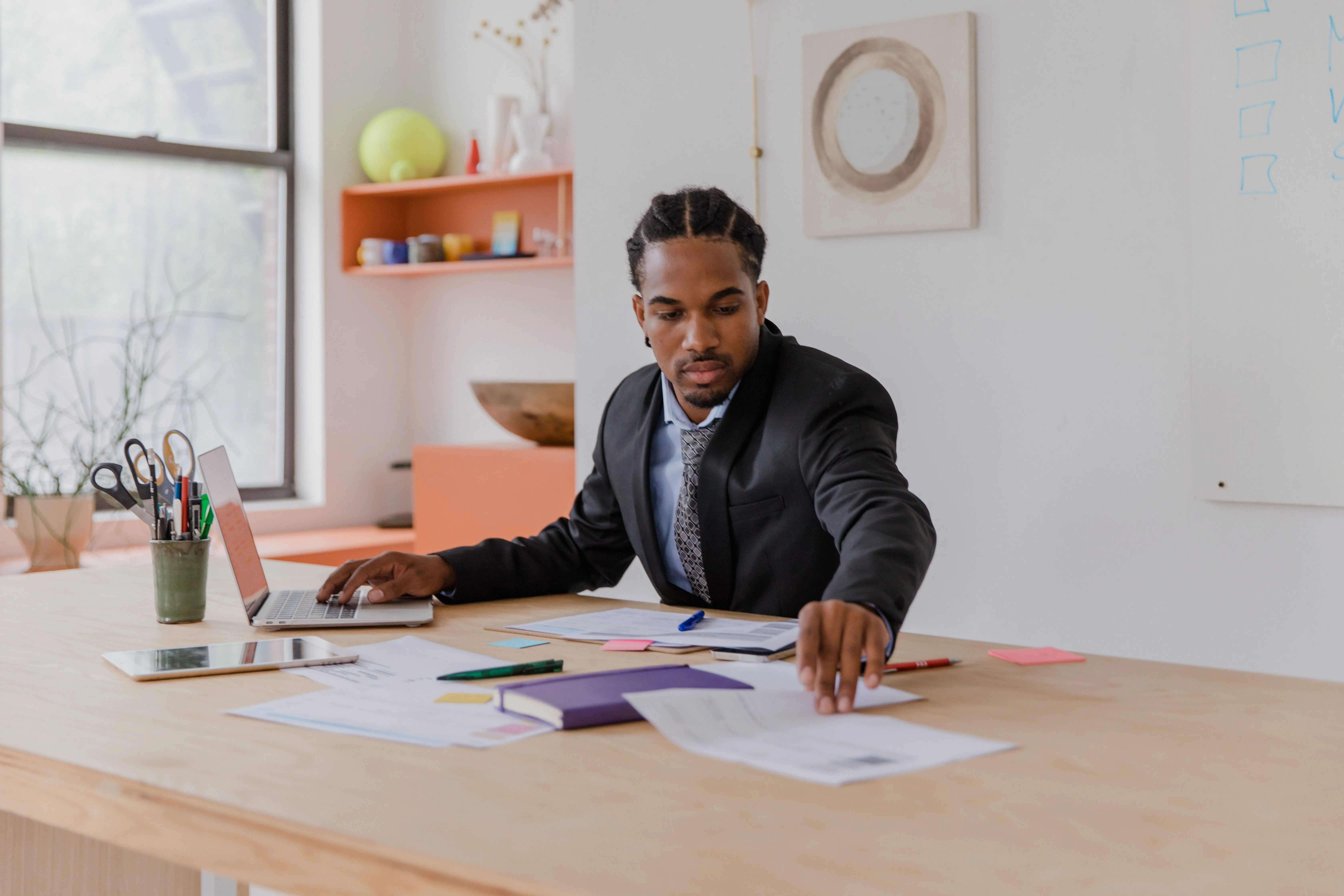 A business owner working alone at a large desk, laying out paperwork beside an open laptop.